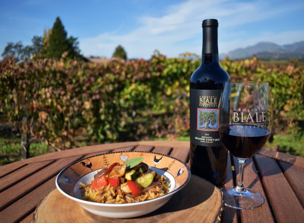 dish filled with orzo and vegetables on wooden table accompanied by a bottle of Biale wine and filled wine glass with Biale logo