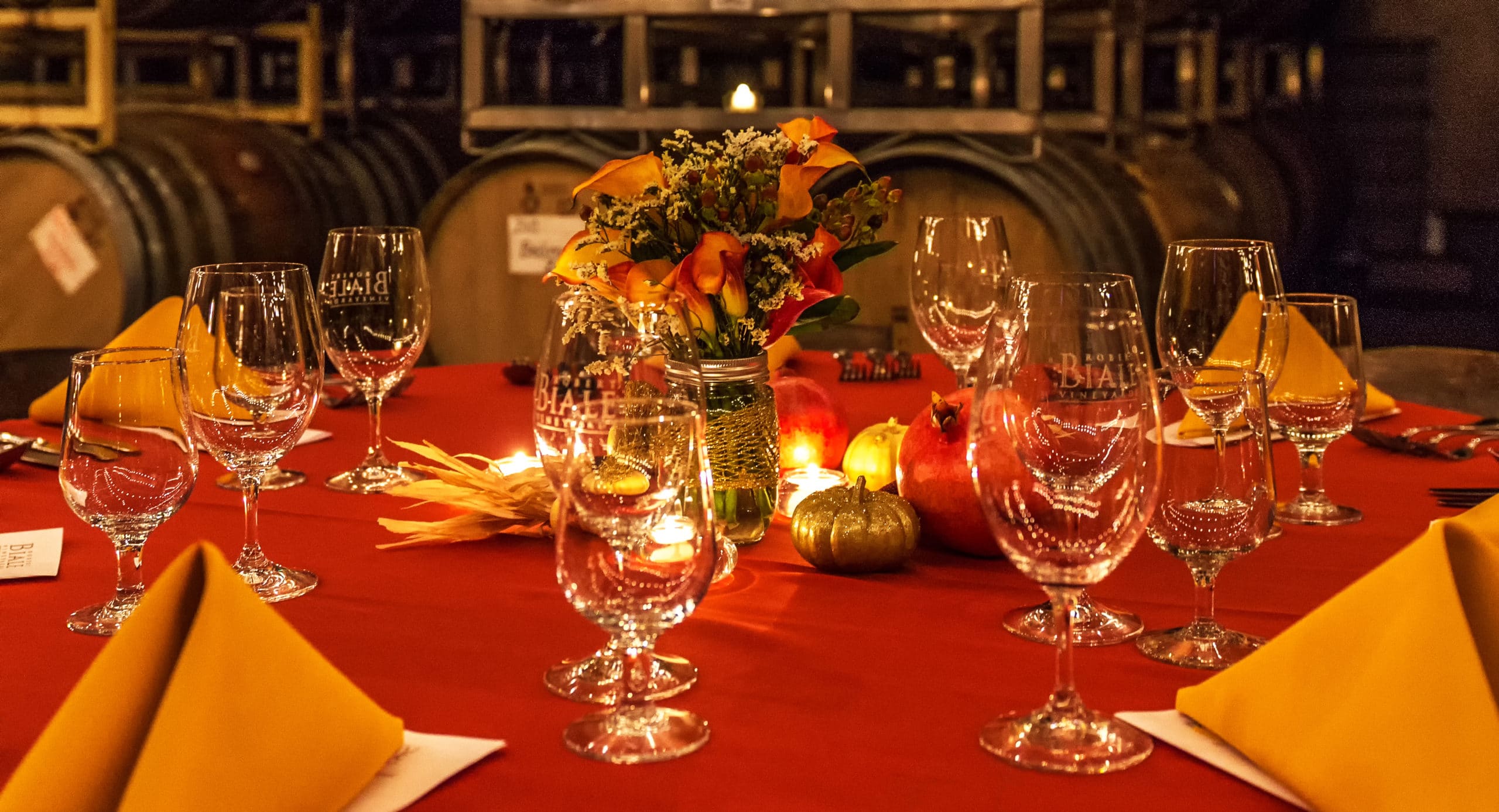 tablescape with red tablecloth and gold napkins with glasses and centerpieces, set in the Biale wine cellar