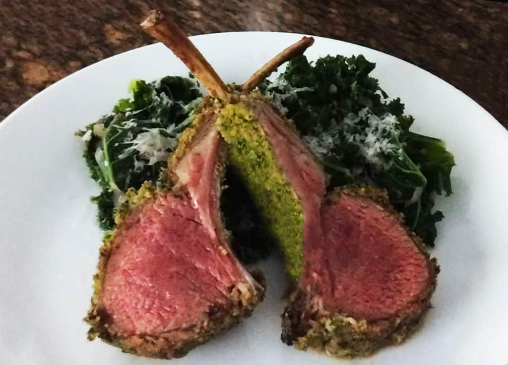 Lamb rack dish served with kale salad topped with shaved cheese plated on white plate