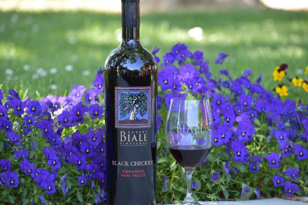 bottle and full glass of Biale Vineyards Black Chicken Zinfandel against a background of purple flowers