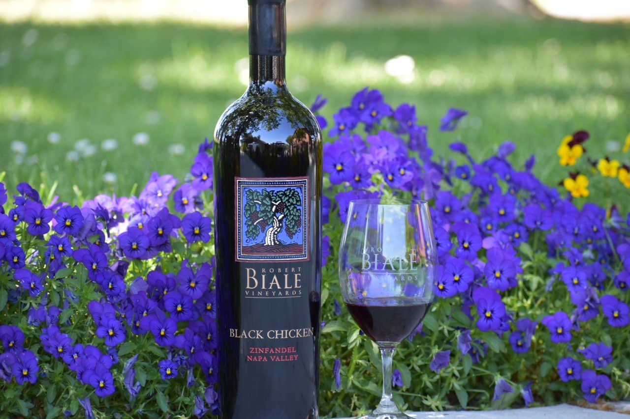 bottle and full glass of Biale Vineyards Black Chicken Zinfandel against a background of purple flowers